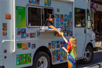 A child reaches for a treat from an ice cream vendor at First Friday